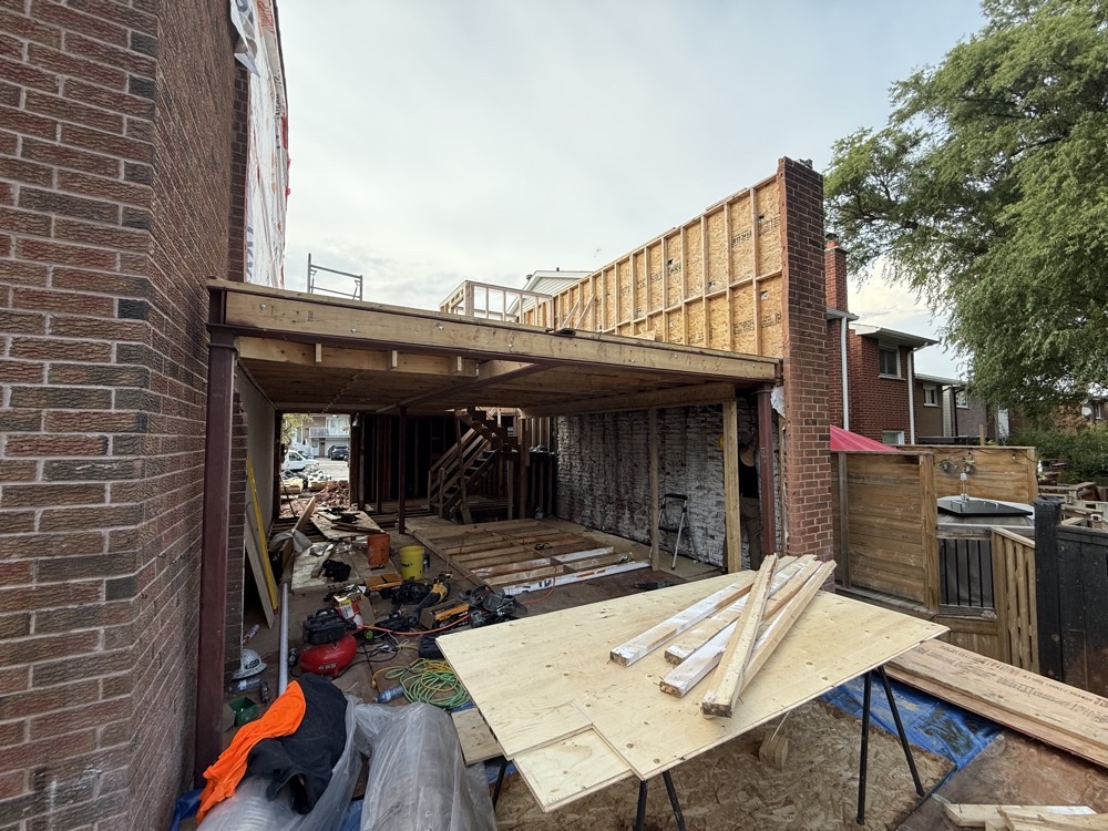 Rear structural demolition — brick house with rear wall removed, steel beam carrying the second-storey addition, first floor gutted to studs